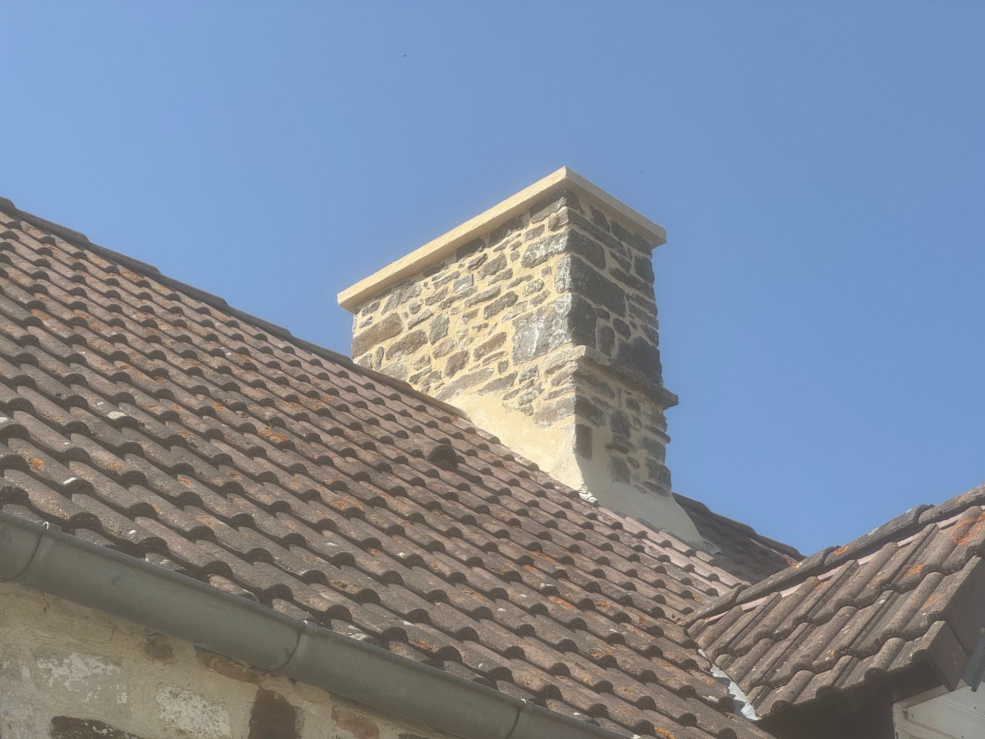 Cheminée en pierre sur un toit de tuiles se détachant sur un ciel bleu