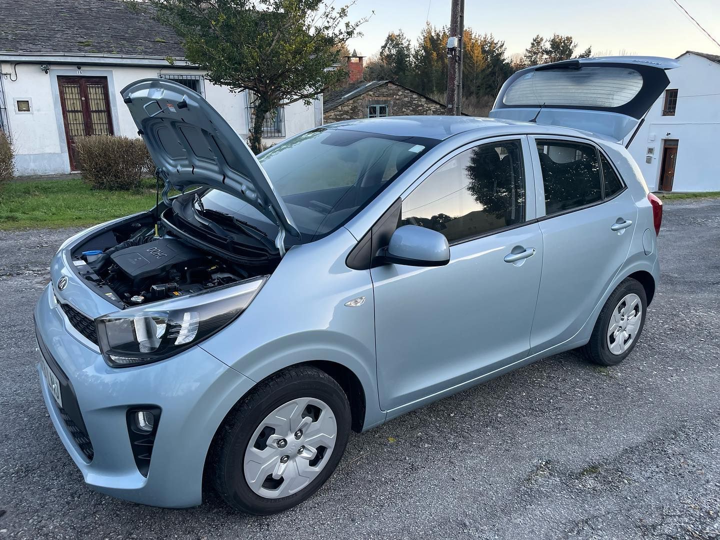 Un coche con el capó levantado está estacionado delante de una casa.