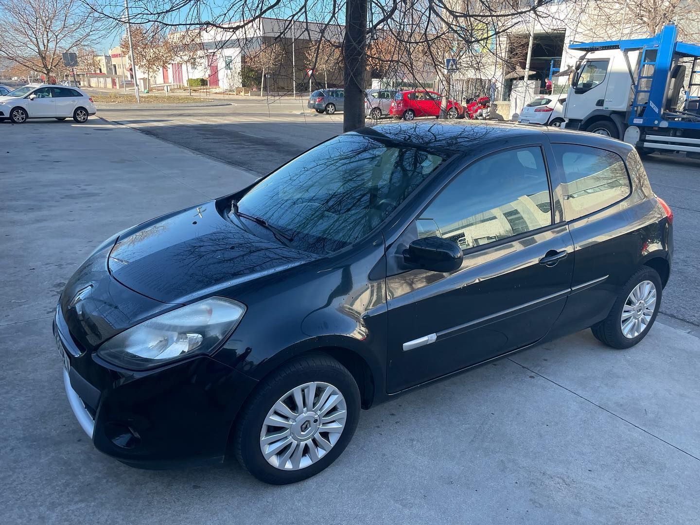 Un coche negro está estacionado en un estacionamiento al lado de un árbol.