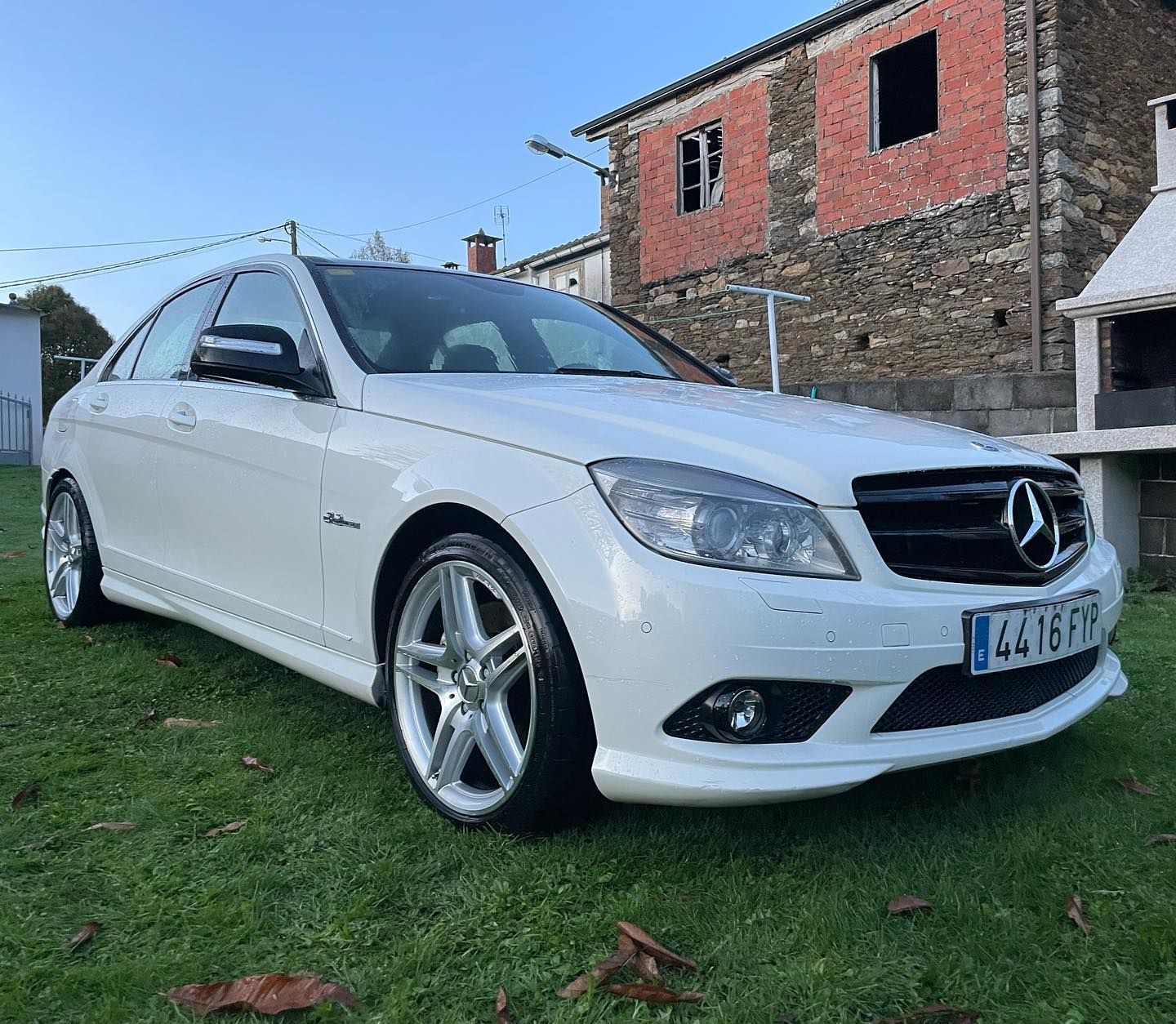 Un Mercedes Benz blanco está estacionado en el césped frente a un edificio de piedra.