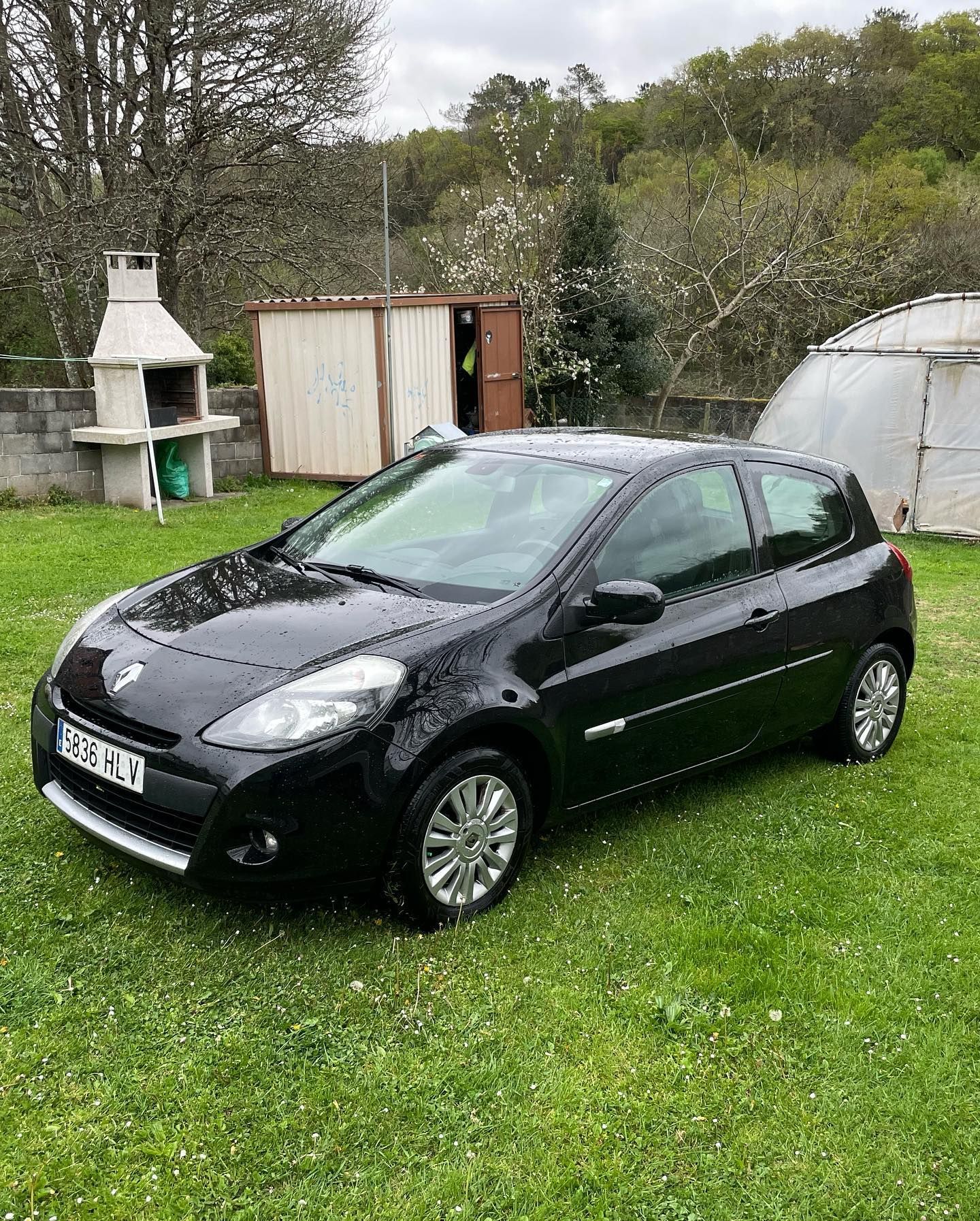 Un coche negro está aparcado en un campo de hierba al lado de una parrilla.