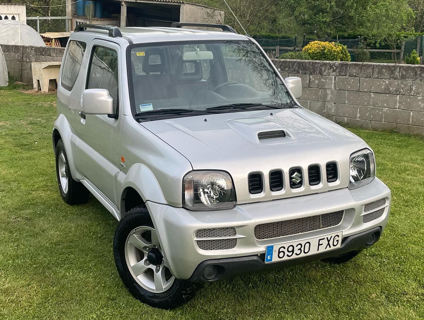 Un Suzuki Jimny plateado está estacionado en un campo de hierba.
