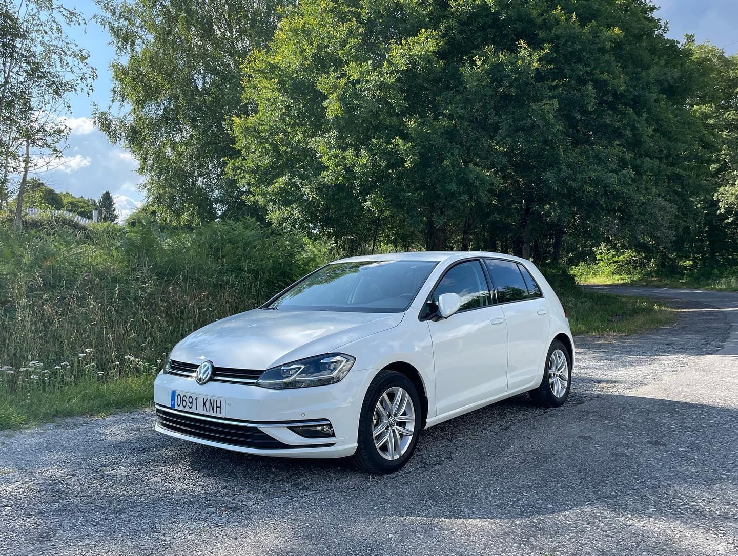 Un Volkswagen Golf blanco está estacionado al costado de la carretera.