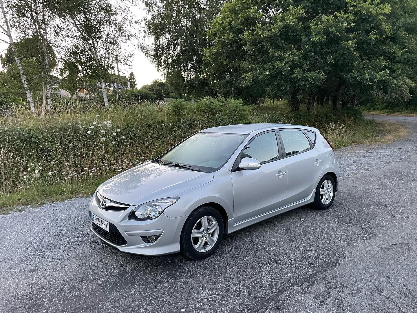 Un coche plateado está aparcado al costado de una carretera.