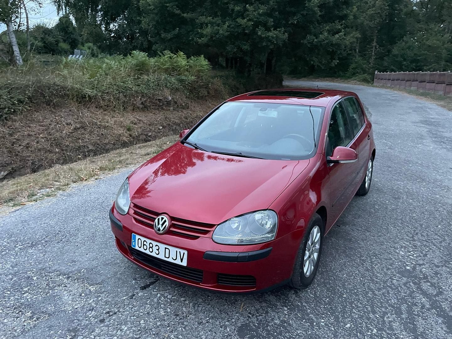 Un Volkswagen Golf rojo está estacionado al costado de un camino de grava.