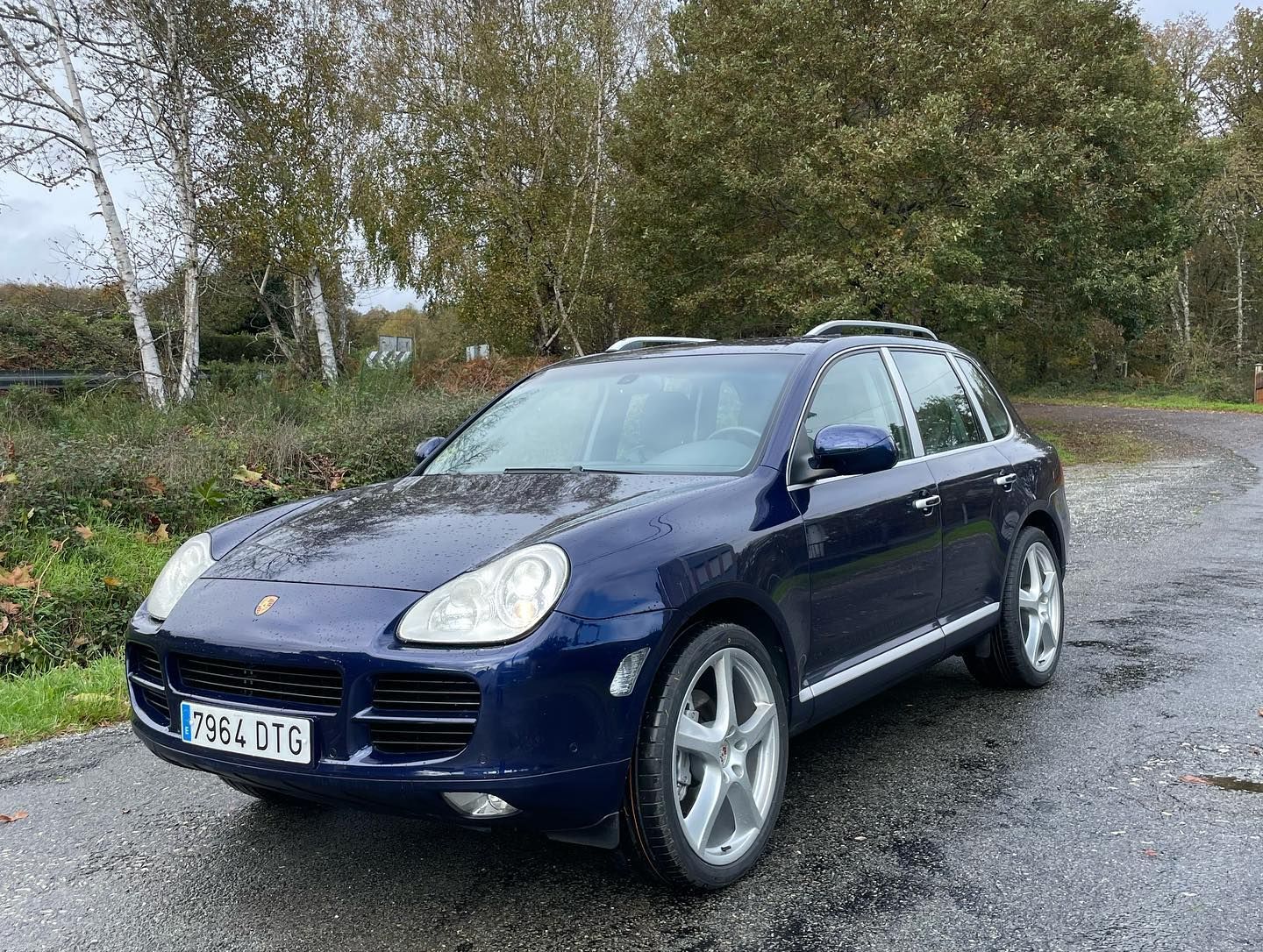 Un Porsche Cayenne azul está estacionado al costado de la carretera.