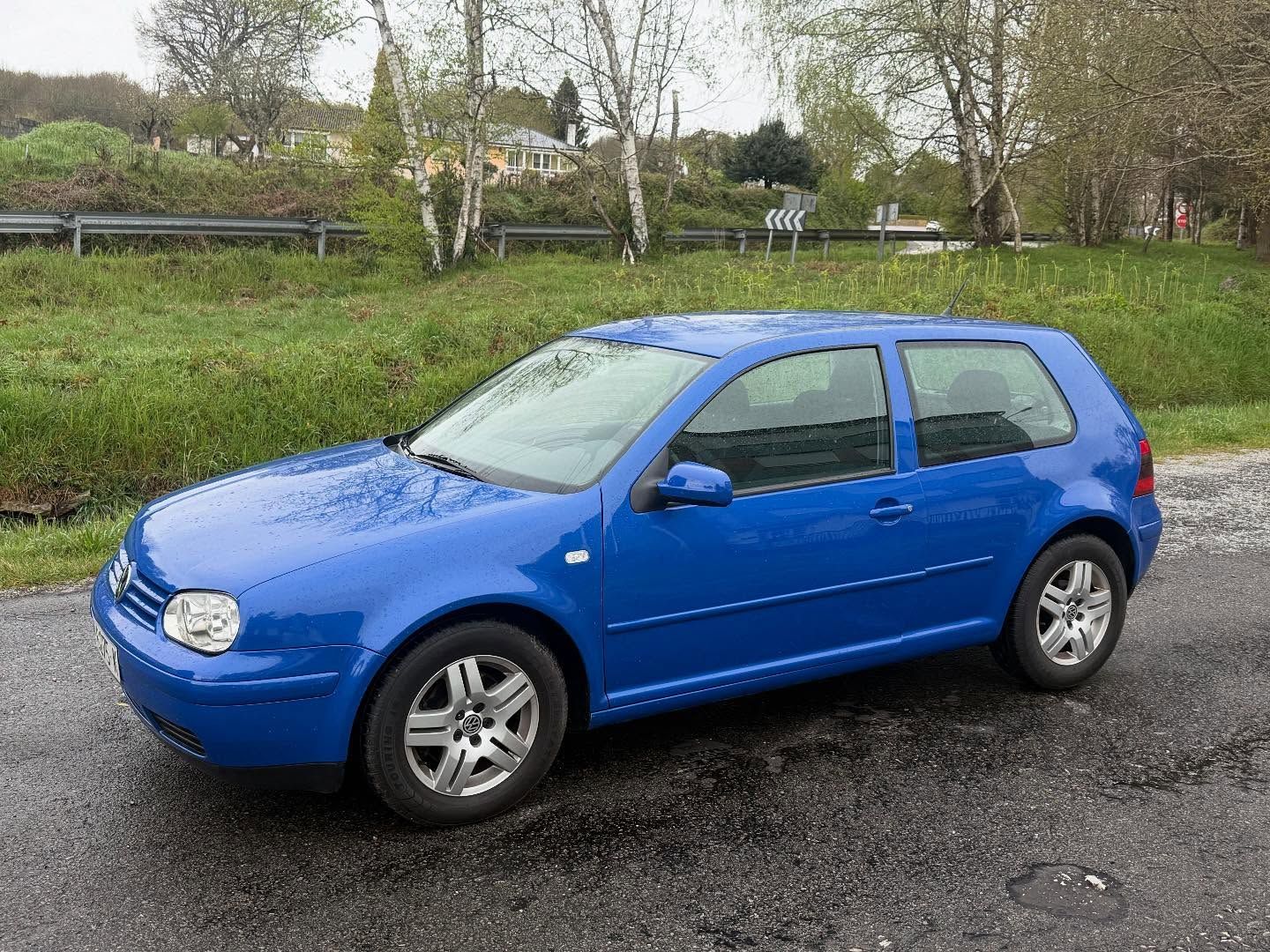 Un Volkswagen Golf azul está estacionado al costado de la carretera.