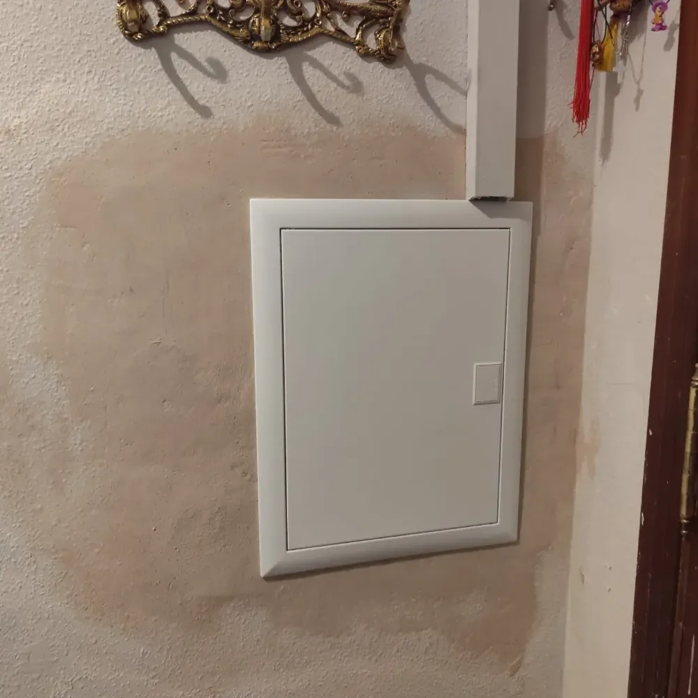 Panel eléctrico blanco montado en la pared sobre una pared beige cerca de una puerta.