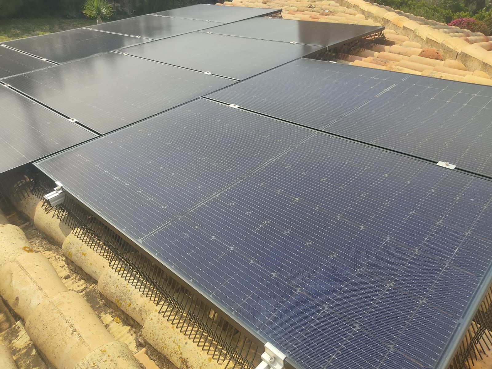 Dos trabajadores instalando paneles solares en un tejado de tejas grises bajo un cielo azul despejado.
