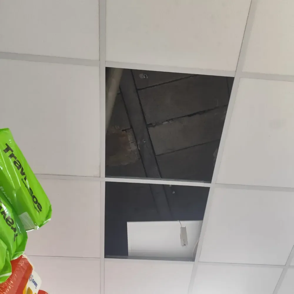 Techo falso que deja al descubierto un espacio oscuro y una lámpara fluorescente colgante en una habitación.
