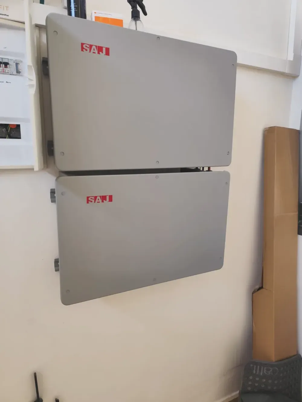 Dos cajas eléctricas grises montadas en la pared con etiquetas rojas en un cuarto de servicio.