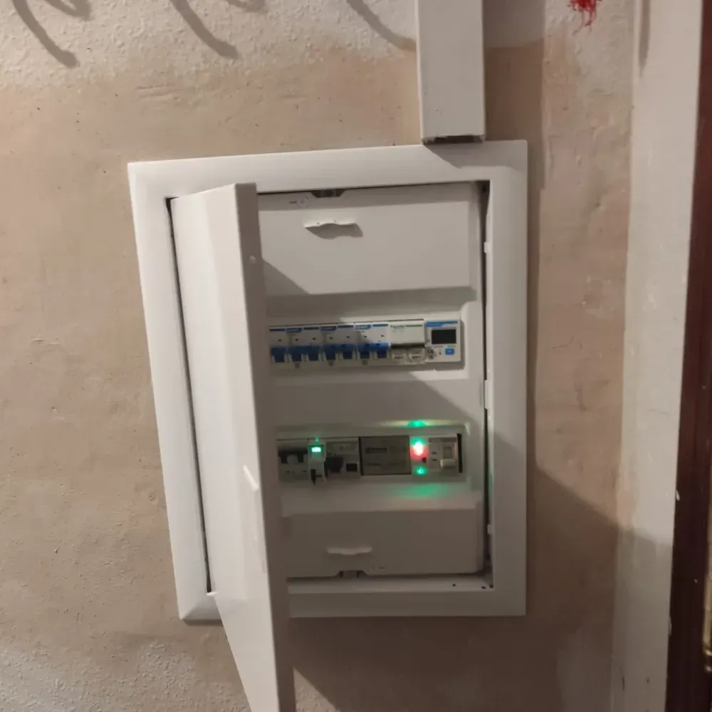 Panel de disyuntores eléctricos abierto con indicadores LED encendidos en un hueco de la pared.