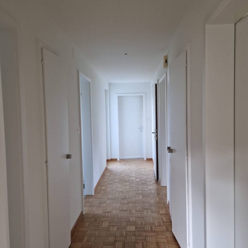 Ein heller, weisser Flur mit mehreren geschlossenen Türen und einem Holzboden.