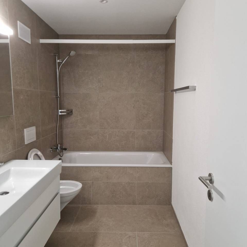 Modernes Badezimmer mit ebenerdiger Badewanne, Dusche, Waschbecken, WC und beigefarbenen Fliesen an Wänden und Boden.