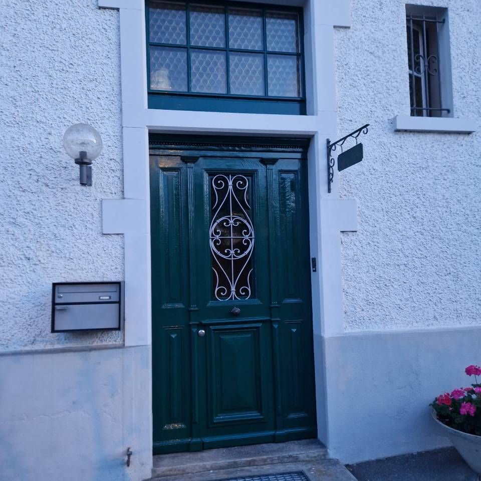 Dunkelgrüne Eingangstür mit Zierglas in einer weissen Stuckfassade.