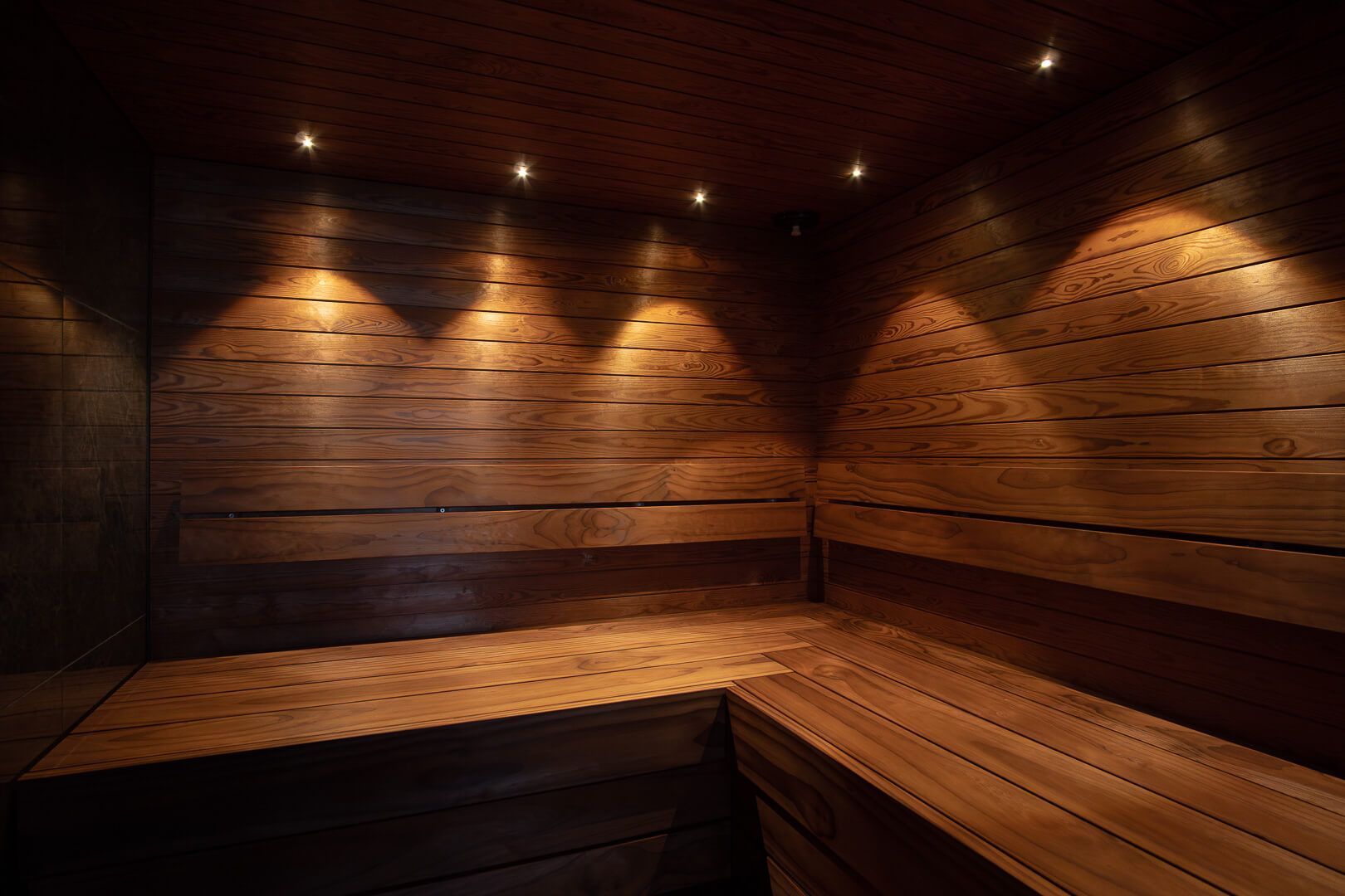 Puupaneelilla verhoiltu sauna, jossa on lämmin valaistus ja puiset penkit seinien varrella