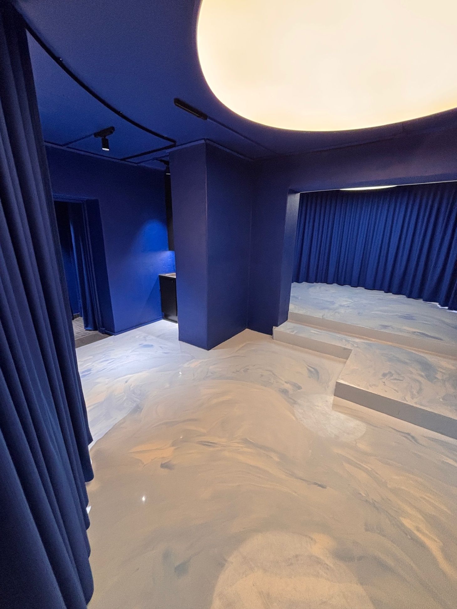 Sininen teatterimainen huone, jossa on verhoillut seinät, kaarevat portaat ja hohtava pyöreä kattovalaisin