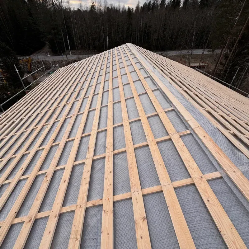 Rakenteilla oleva katto, jossa puiset rimoja harmaan vedenpitävän kalvon päällä, harjalta katsottuna.