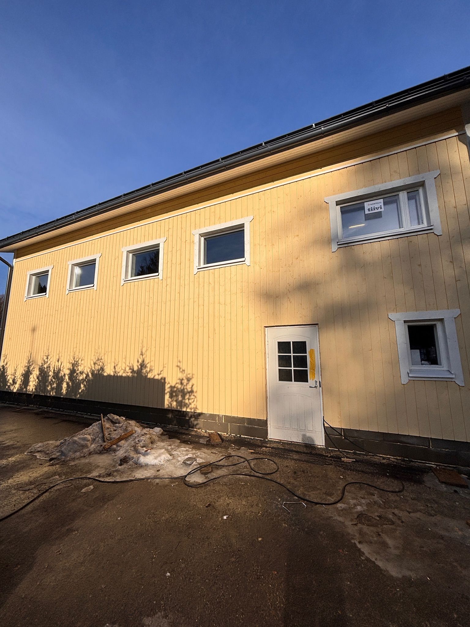 Keltainen rakennuksen ulkoasu pienillä ikkunoilla ja valkoisella ovella päällystetyllä tontilla auringonlaskun aikaan