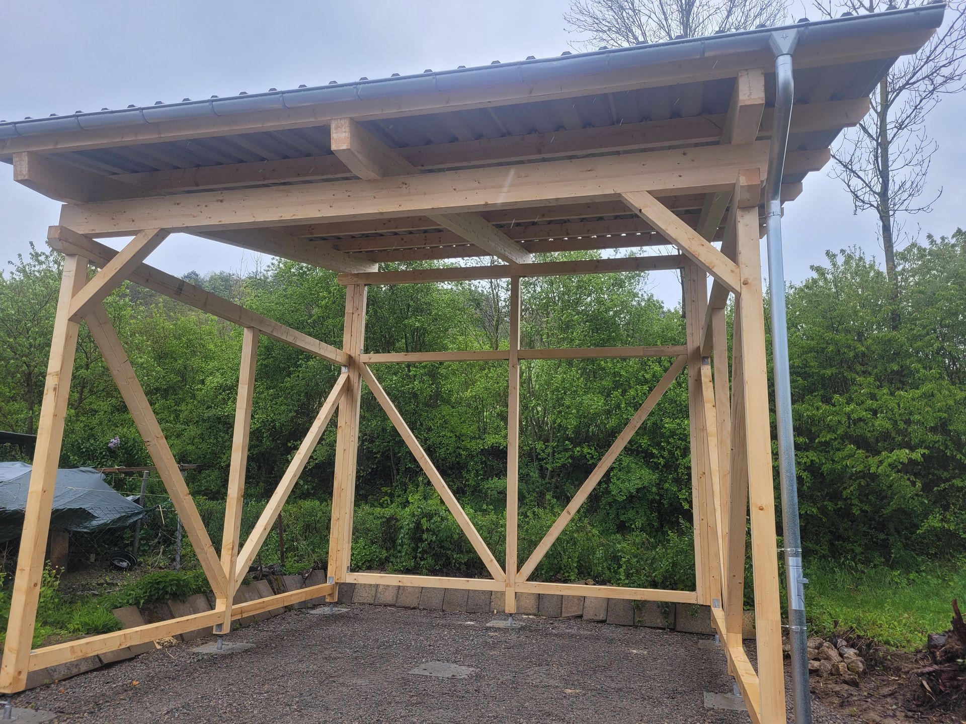 Eine Person baut eine hölzerne Pergola auf einer modernen Terrasse mit Kies und Gartengestaltung.