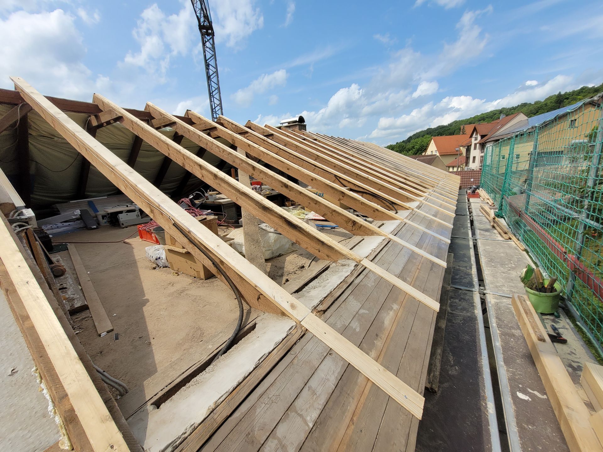 Ein Dachdecker verlegt unter blauem Himmel dunkelgraue Dachziegel auf einem hölzernen Dachstuhl.
