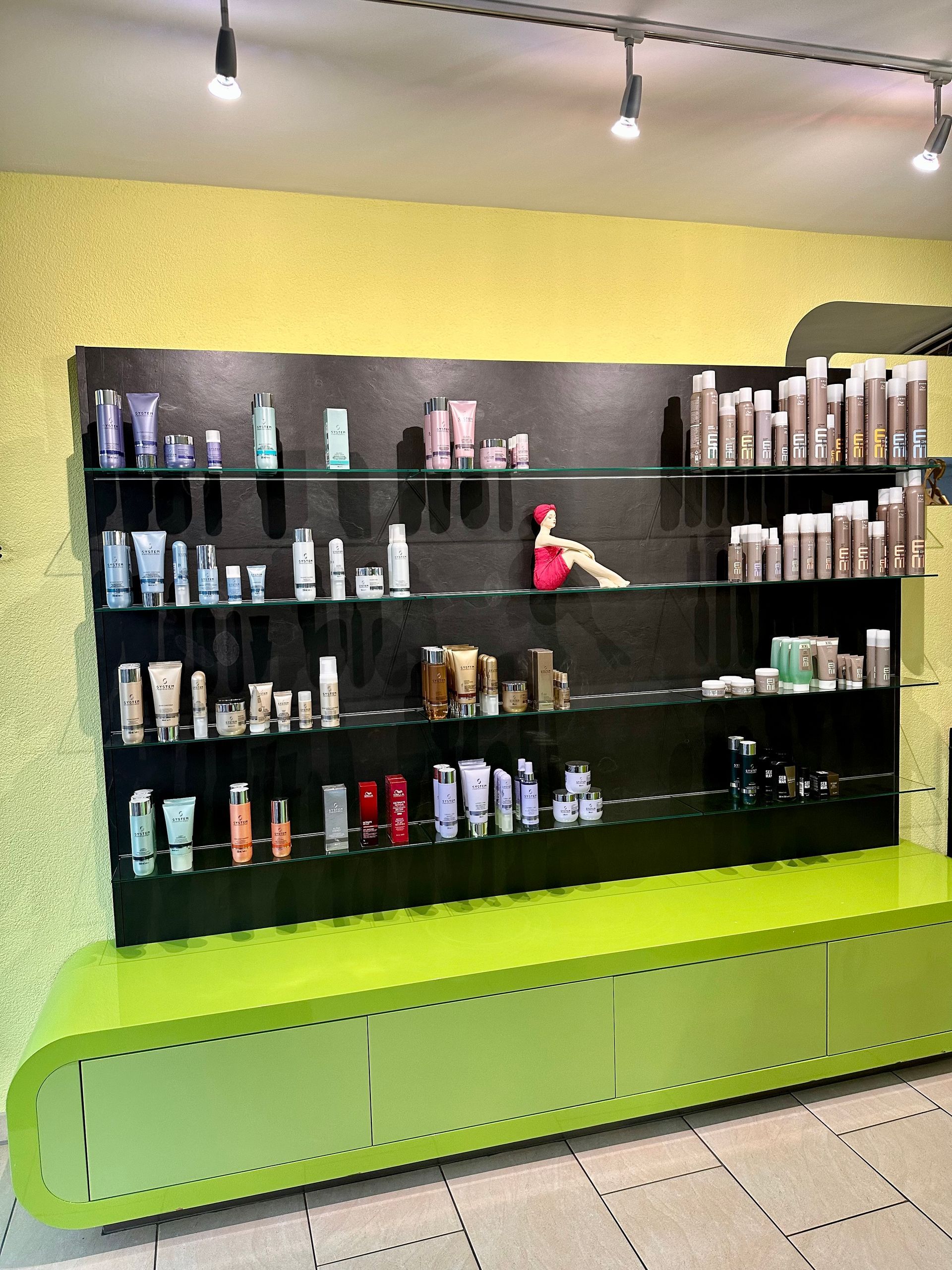 Interieur eines Friseursalons mit schwarzen Stühlen, weissen Waschbecken, grünem Tresen und Produktauslage.