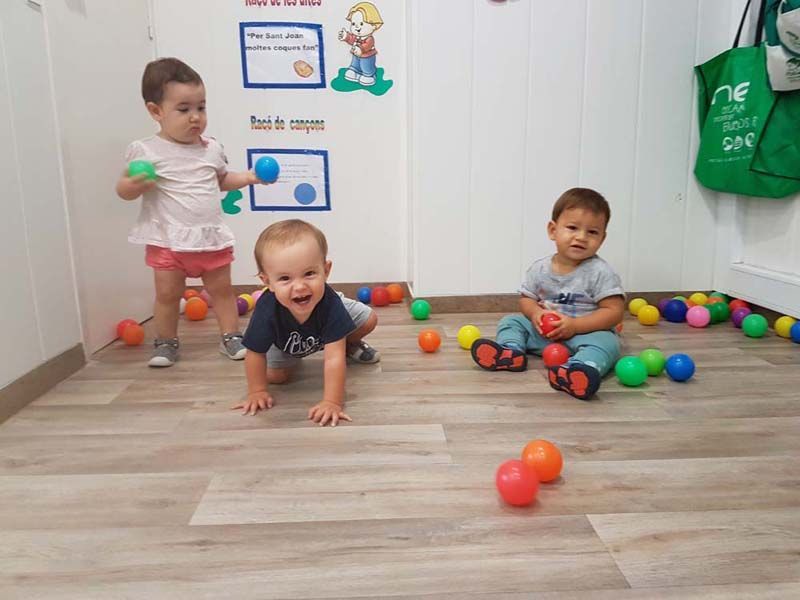 Tres niños están jugando con pelotas en el suelo de una habitación.