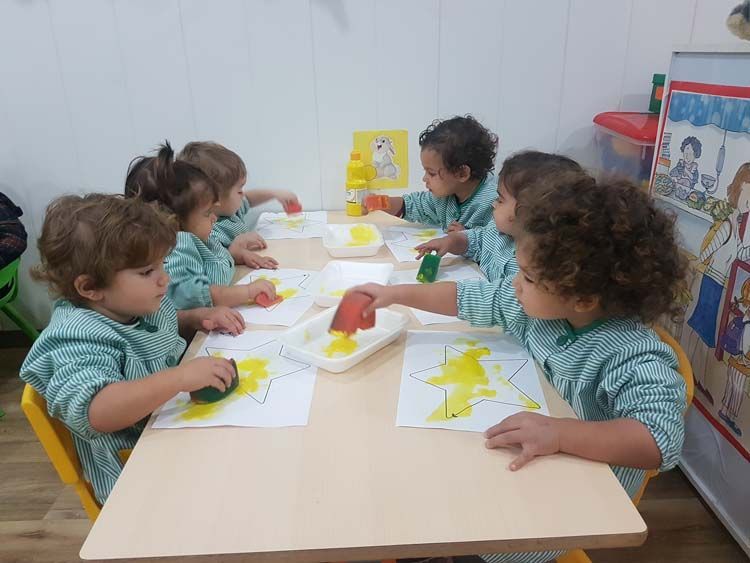 Un grupo de niños pequeños está sentado en una mesa jugando con pintura.