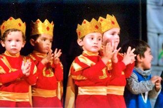 Un grupo de jóvenes vestidos con trajes y coronas rojas y doradas aplauden.