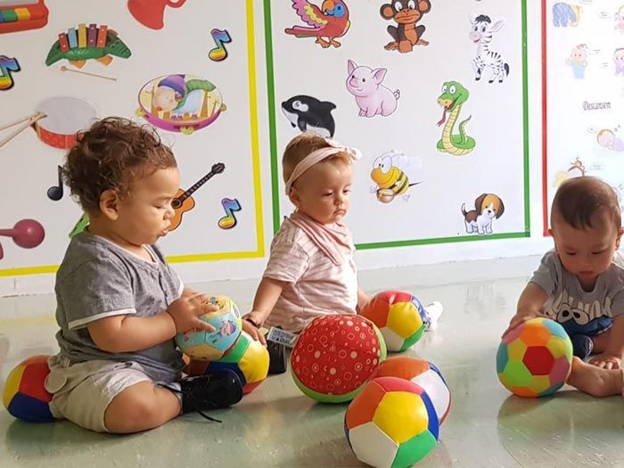Tres bebés están sentados en el suelo jugando con pelotas.