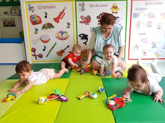 Un grupo de bebés está jugando con juguetes sobre una alfombra verde.