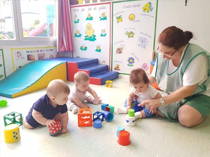 Una mujer está sentada en el suelo con tres bebés jugando con juguetes.