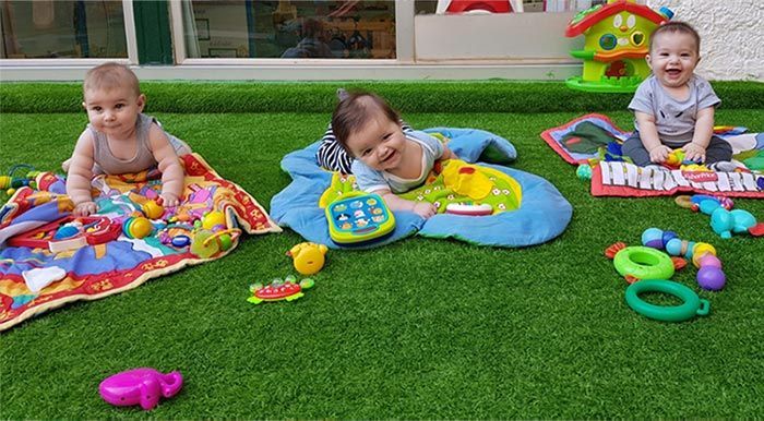 Tres bebés están jugando con juguetes en el césped.