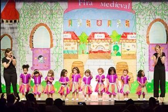 Un grupo de niños está bailando en un escenario frente a un castillo.