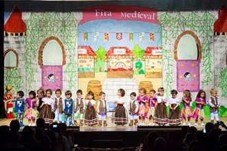 Un grupo de niños está de pie en un escenario frente a un cartel que dice medieval