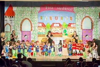 Un grupo de niños están de pie en un escenario frente a un cartel que dice fina medieval