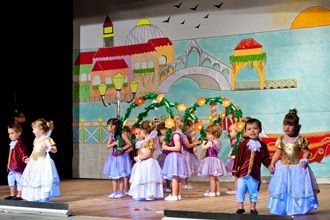 Un grupo de niños está de pie en un escenario frente a una pintura.