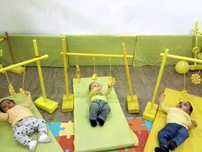 Tres bebés están acostados sobre colchonetas amarillas en una habitación con juguetes amarillos.