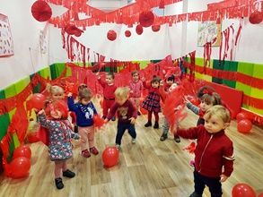 Un grupo de niños está de pie en una habitación llena de globos rojos.