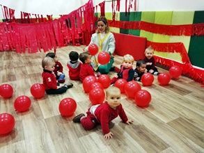 Un grupo de bebés está jugando con globos rojos en una habitación.