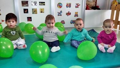 Un grupo de bebés está sentado en una colchoneta con globos verdes.