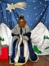 Un hombre vestido de rey está sentado delante de un belén.