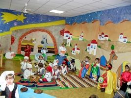 Un grupo de niños está sentado en el suelo delante de un cuadro de un belén.