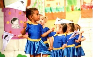 Un grupo de jovencitas vestidas de azul sostienen banderas.