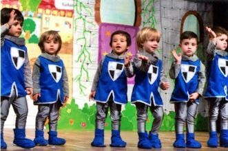 Un grupo de niños vestidos con trajes de caballeros azules están de pie en un escenario.