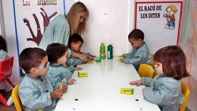 Un grupo de niños están sentados en una mesa frente a un cartel que dice el raco de les dites