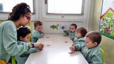 Un grupo de bebés está sentado en una mesa con una maestra.