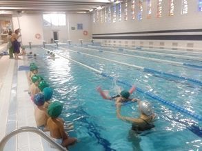 Un grupo de niños está nadando en una gran piscina cubierta.
