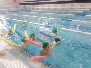 Un grupo de niños están nadando en una piscina con fideos de espuma.