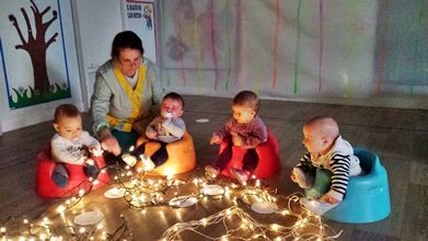 Un grupo de bebés está sentado en el suelo en una habitación con luces navideñas.